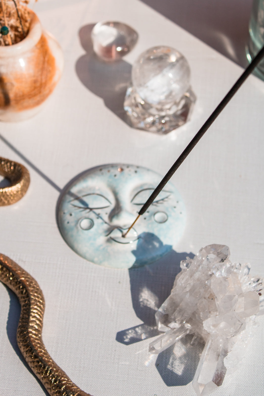 Lifestyle shot shows a celestial moon incense holder holds a stick of incense. Various healing crystals and decorative accents surround the spread.