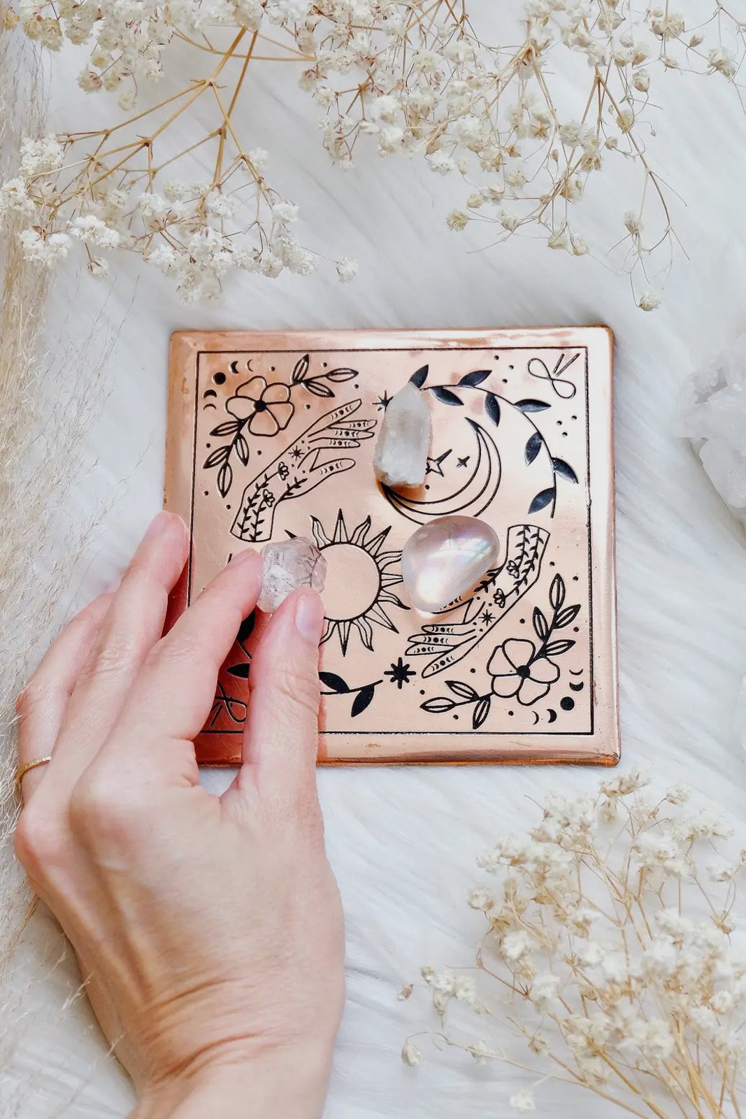 hand places quartz crystals atop a copper plate etched with mystical designs