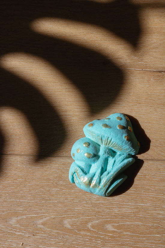 organic bath bomb shaped like mushroom and painted teal blue with a monstera leaf shadow on the background