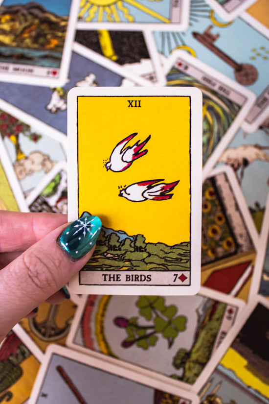 Pixie's Astounding Lenormand cards. This deck features artwork reminiscent of traditional Tarot archetypes, but in a simpler fashion. A hand holds a card featuring two birds.