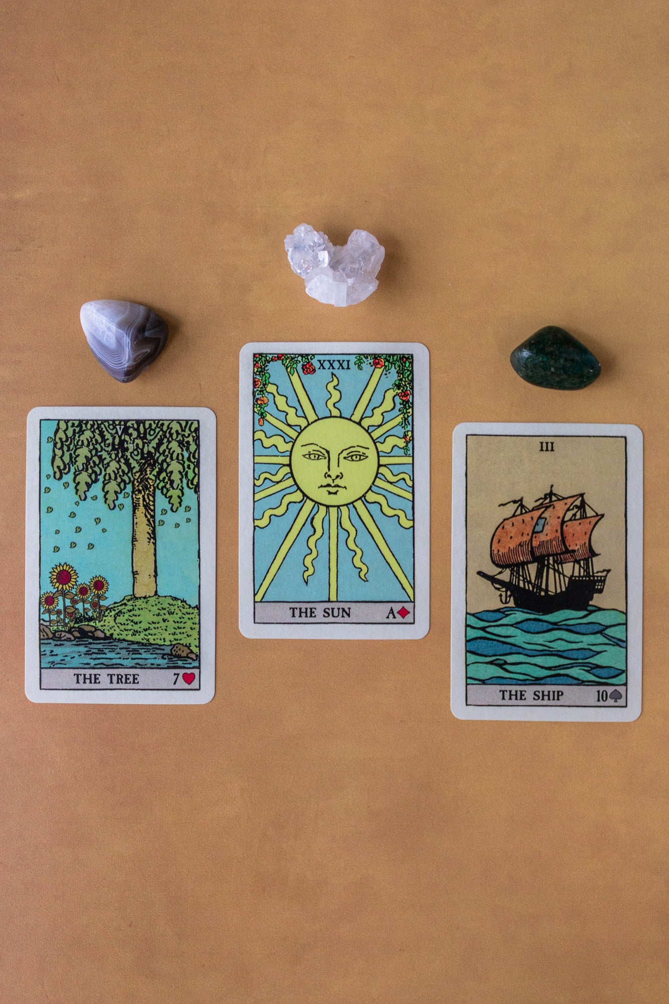 Three cards from Pixie's Astounding Lenormand deck are spread out: The Tree, The Sun, and The Ship. Three crystals lay above them.